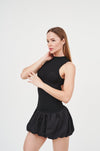 Sleek black mini dress with turtleneck and ruffle trim, worn by young woman with long hair against plain background.