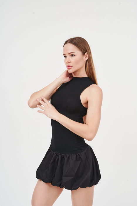 Sleek black mini dress with turtleneck and ruffle trim, worn by young woman with long hair against plain background.