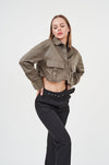 Stylish woman wearing olive crop jacket and black wide-leg pants, posing against plain white background