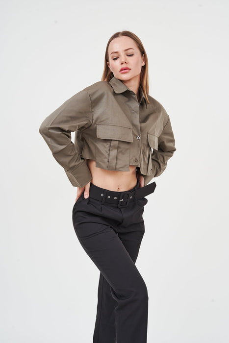 Stylish woman wearing olive crop jacket and black wide-leg pants, posing against plain white background