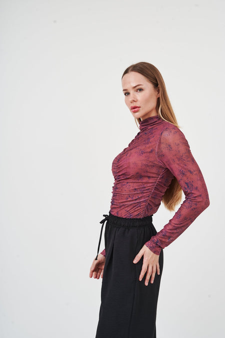 Elegant burgundy floral embroidered blouse worn by a fashionable woman against a plain background.