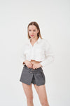 Stylish mini skirt with built-in shorts, featuring a white collared blouse on a young woman against a plain background.