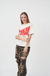 Vibrant Graphic White T-Shirt for Modern Women
Stylish woman wearing a white t-shirt with bold "New York" graphic, paired with leopard print pants.